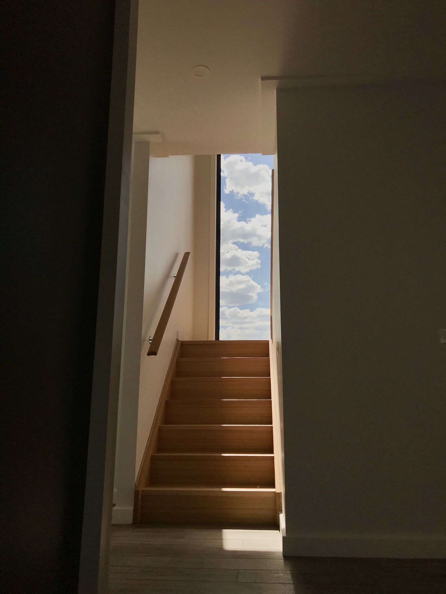 Timber staircase rising toward a tall window and sky