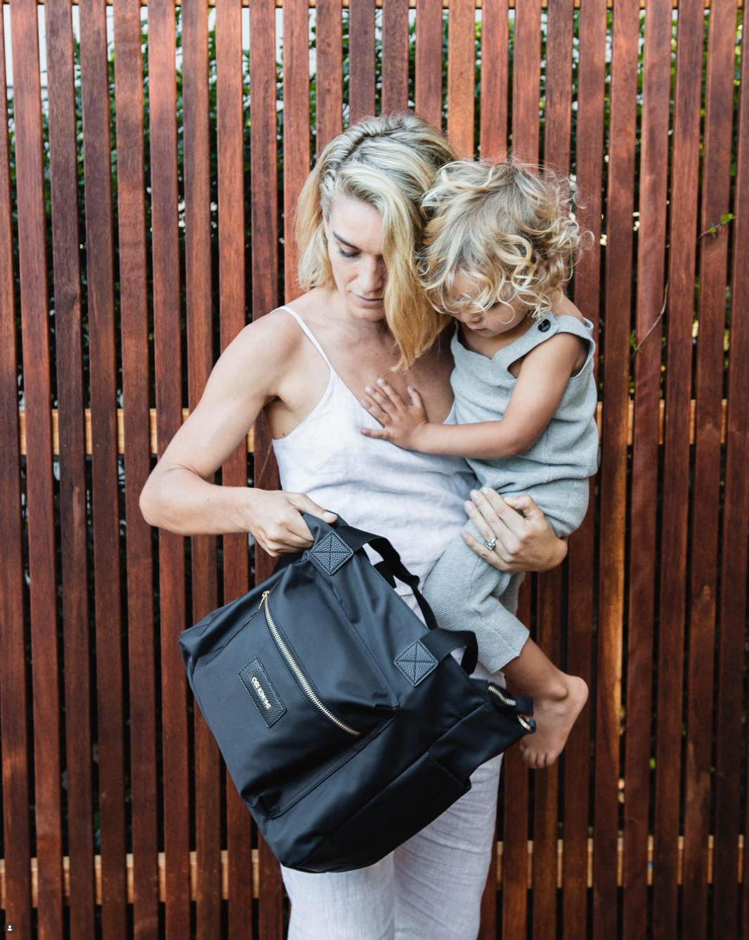 Mother carrying a child and an Obi Kinomi black backpack
